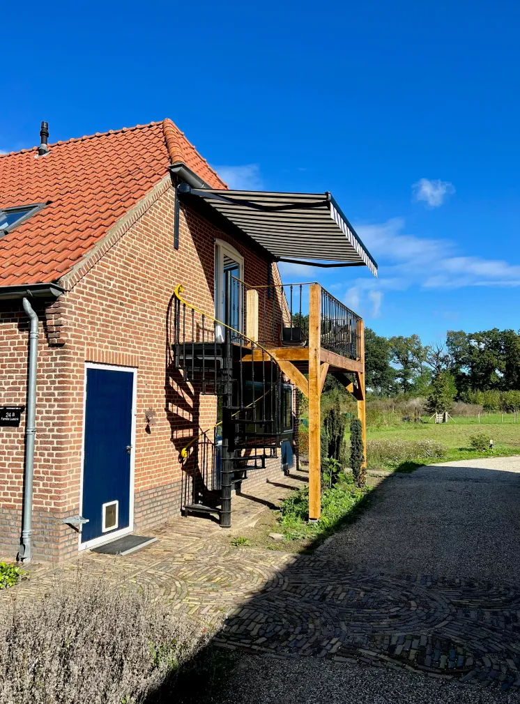 Zijaanzicht van de boerderij met balkon en blauwe deur